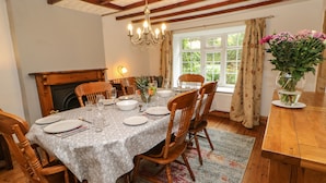 Comedor con una mesa de madera dispuesta para cuatro, rodeada de sillas de madera, un candelabro y una ventana con cortinas.