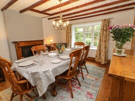 A dining room with a wooden table set for four, surrounded by wooden chairs, a chandelier, and a window with curtains.