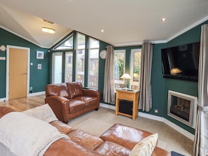A living room with a brown leather sofa, a small wooden side table, a fireplace, and a television mounted on the wall.