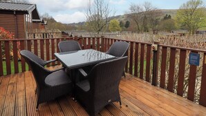 A wooden deck with wicker furniture and a view of a rural landscape. - Elder Lodge (Windermere)