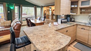 A modern kitchen with granite countertops, wooden cabinets, and a dining area with leather chairs. - Elder Lodge (Windermere)