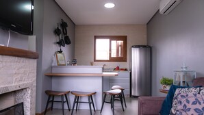 A compact living space with a kitchen area, a dining bar, and a seating area with a sofa and two stools. - Refúgio dos Coiotes (Cambara do Sul)