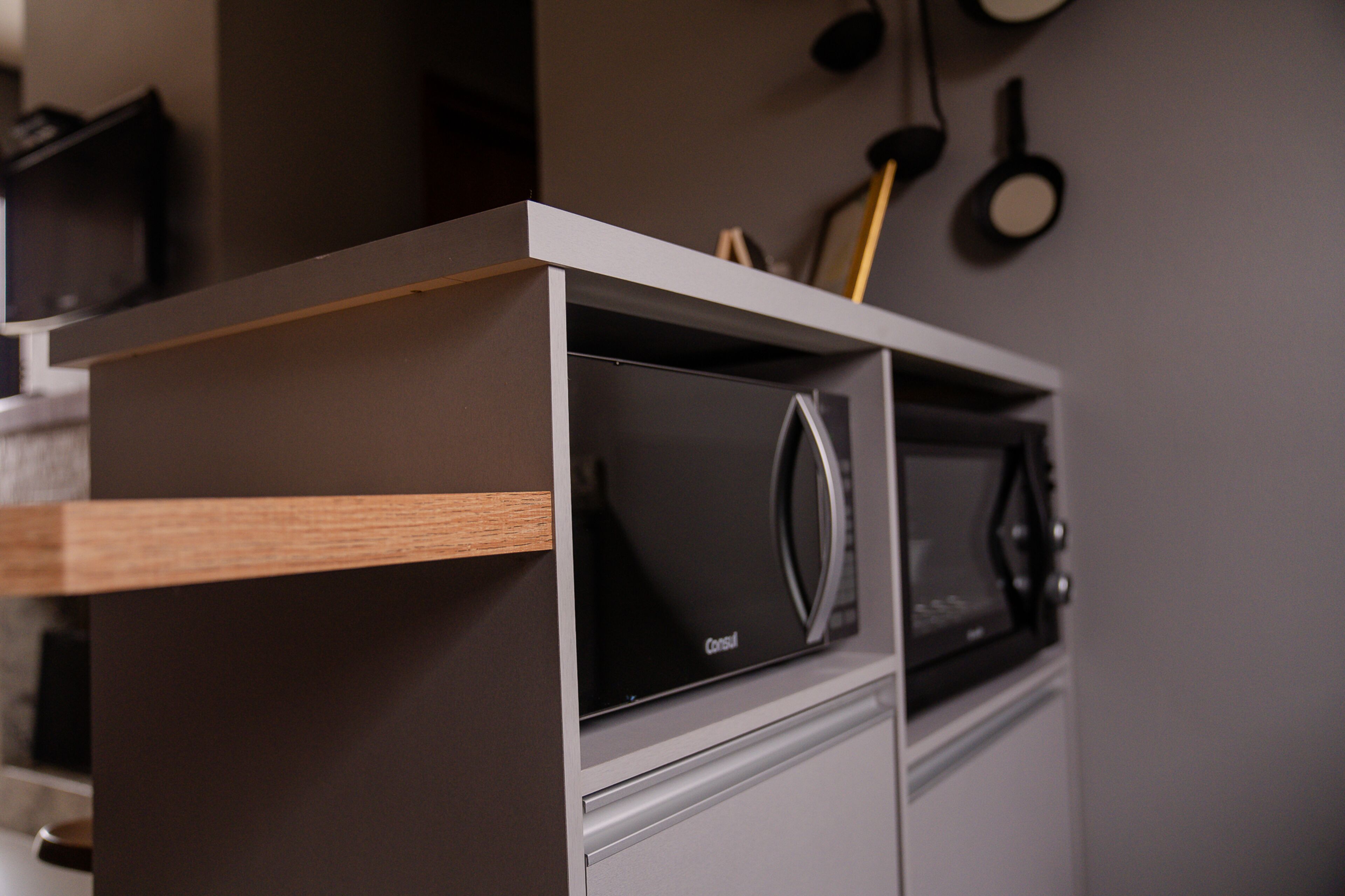 A kitchen with a built-in microwave and oven, a wooden shelf, and a hanging pot rack.
