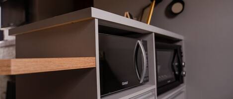 A kitchen with a built-in microwave and oven, a wooden shelf, and a hanging pot rack.