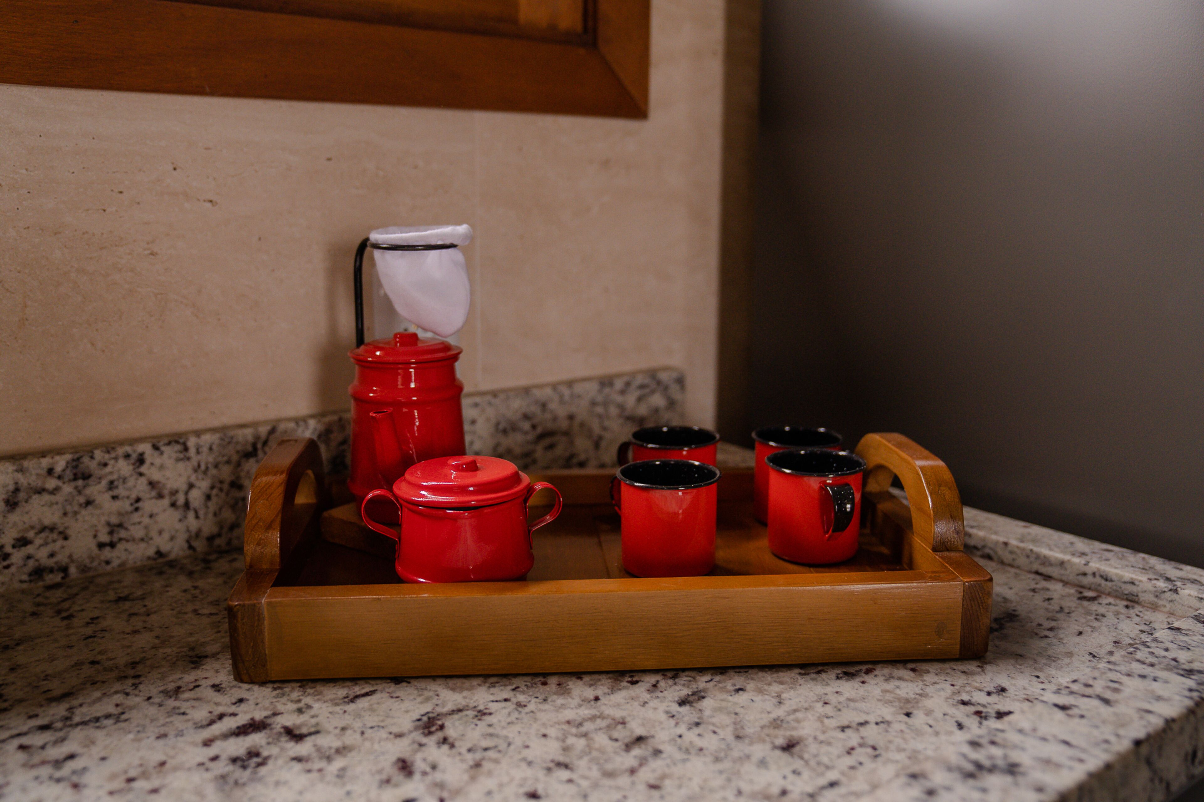 Un plateau en bois avec des théières et des tasses rouges, posé sur un comptoir en granit.
