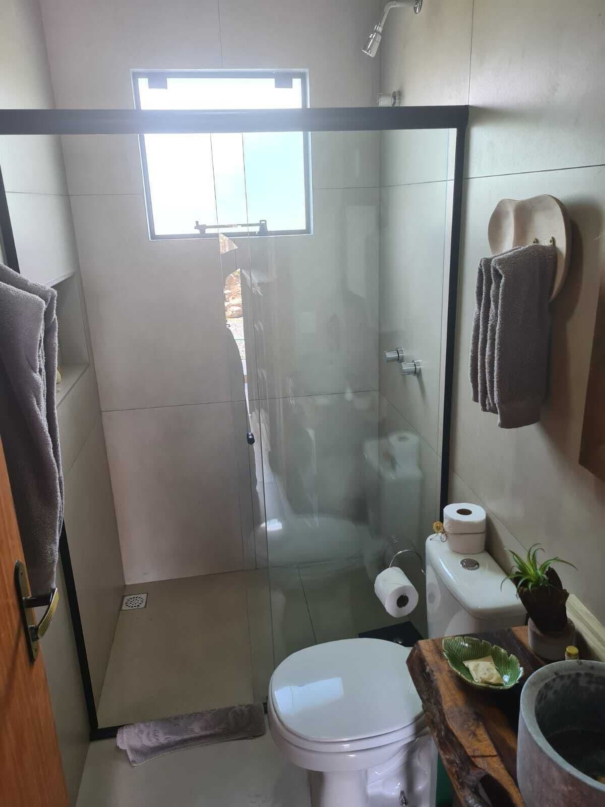 Ein Badezimmer mit einer gläsernen Duschkabine, Toilette, Waschbecken mit Holzplatte und einem kleinen Topfpflanzen.
