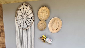 A cozy corner with a wooden bench, macrame wall hanging, woven hats, and a small decorative plant. - Refúgio dos Coiotes (Cambara do Sul)