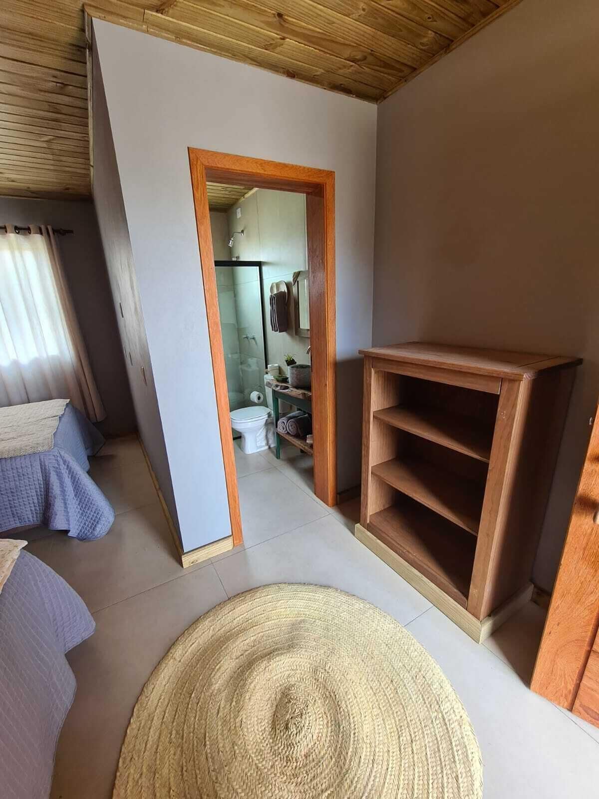 Een kamer met een houten plafond, een groot geweven vloerkleed, een houten kast en een deur naar een badkamer.