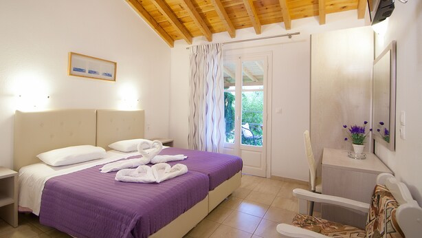 Un dormitorio con cama, mesita de noche, silla, escritorio, ventana con cortinas y techo de madera.