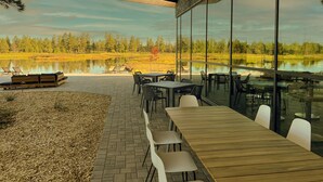 An outdoor patio with tables and chairs, overlooking a lake and forest. - Backland Luxury Nature Resort - Grand Canyon (Williams)