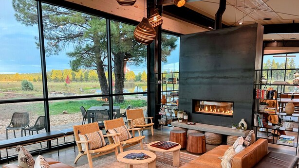 A modern living room with large windows, a fireplace, and a bookshelf. - Backland Luxury Nature Resort - Grand Canyon (Williams)