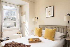 A hotel room with a bed, bedside lamps, a framed picture, and a breakfast tray on the bed.