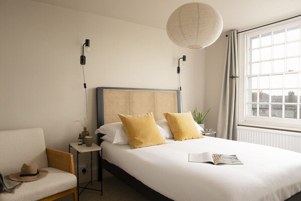 A hotel room with a large bed, a chair, a bedside table with a lamp, and a window with curtains.
