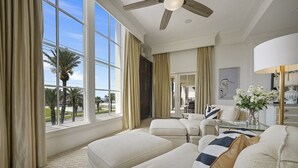 A spacious living room with large windows, a ceiling fan, and a view of palm trees.