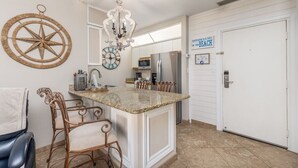 A kitchen with a central island, copper chairs, a chandelier, and a sign that says "HAPPINESS IS A DAY AT THE BEACH". - Beachfront Bar! Restaurant on Site! Spa! Tennis! Beach Service Included! (Miramar Beach)