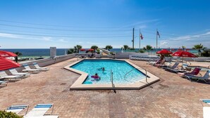 A swimming pool with lounge chairs and umbrellas, surrounded by a tiled deck and a view of the ocean. - Beachfront Bar! Restaurant on Site! Spa! Tennis! Beach Service Included! (Miramar Beach)