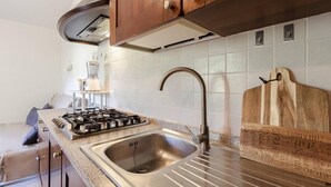 Una cocina con un lavamanos de acero inoxidable, una estufa a gas, armarios de madera y una tabla de cortar de madera.