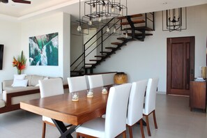 A modern dining area with a wooden table and white chairs, a staircase with a black railing, and a large abstract painting on the wall. - Brand-new Luxury 4 bedroom Villa with unparalleled ocean views from every room (Puerto Vallarta)
