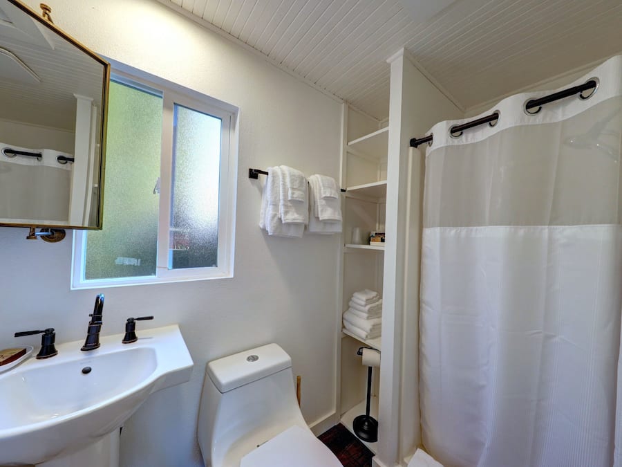 Une salle de bain avec un lavabo blanc, des toilettes, un miroir et un rideau de douche.
