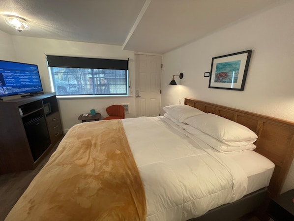 A hotel room with a bed, a desk with a computer, a chair, a window, and a framed picture on the wall. - The Seaview Cottages (Seaview)
