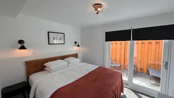 Ein Schlafzimmer mit einem Bett, zwei Nachttischlampen, einer Deckenleuchte, einem Fenster mit Blick auf einen Holzzaun und einem gerahmten Bild an der Wand.