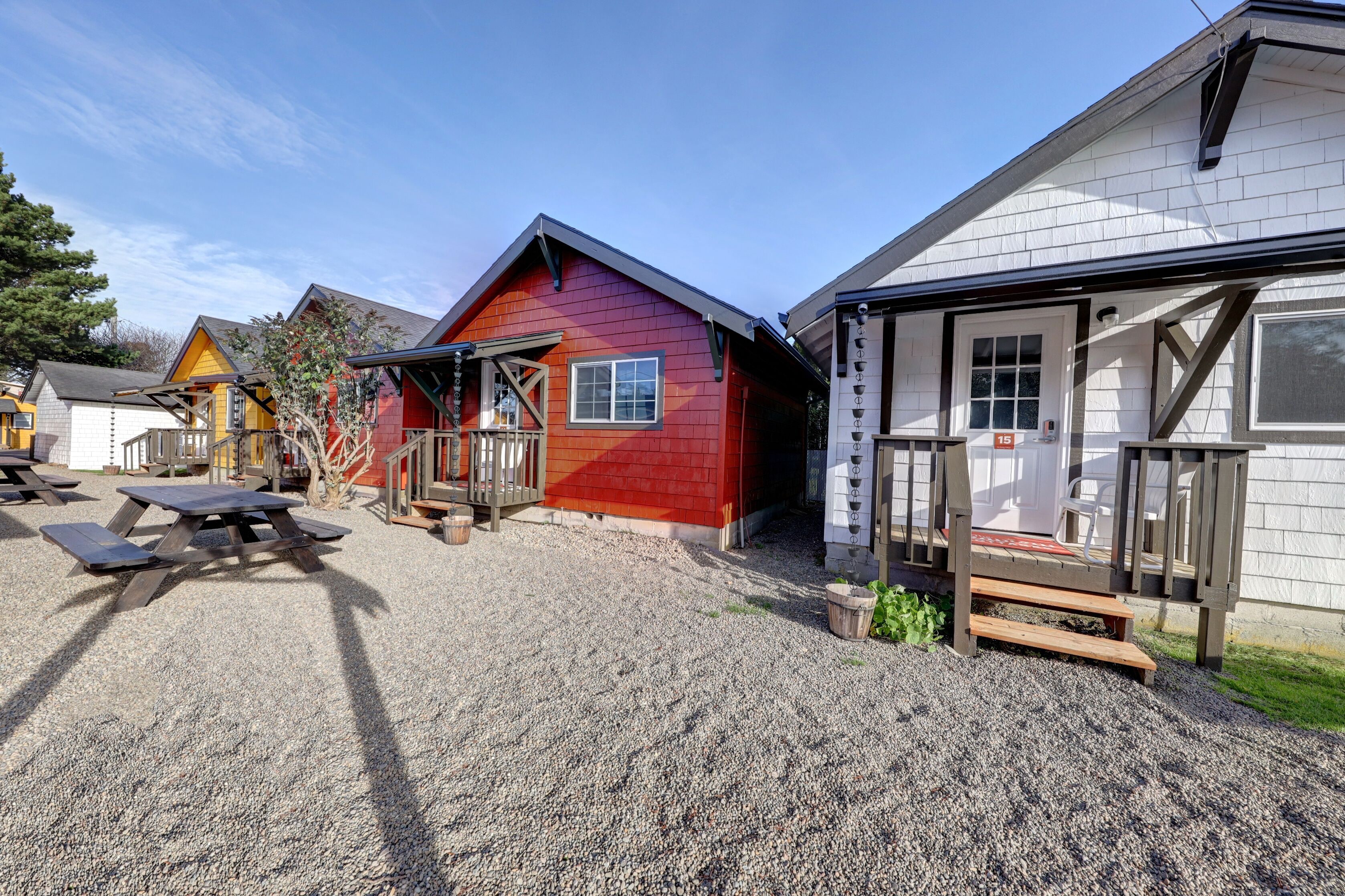 A row of cabins with picnic tables in front, a gravel driveway, and a clear sky.