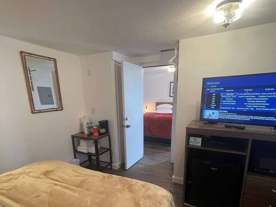 Une chambre d’hôtel équipée d’un lit, d’une télévision, d’un bureau avec un ordinateur et d’une porte donnant sur une autre pièce.