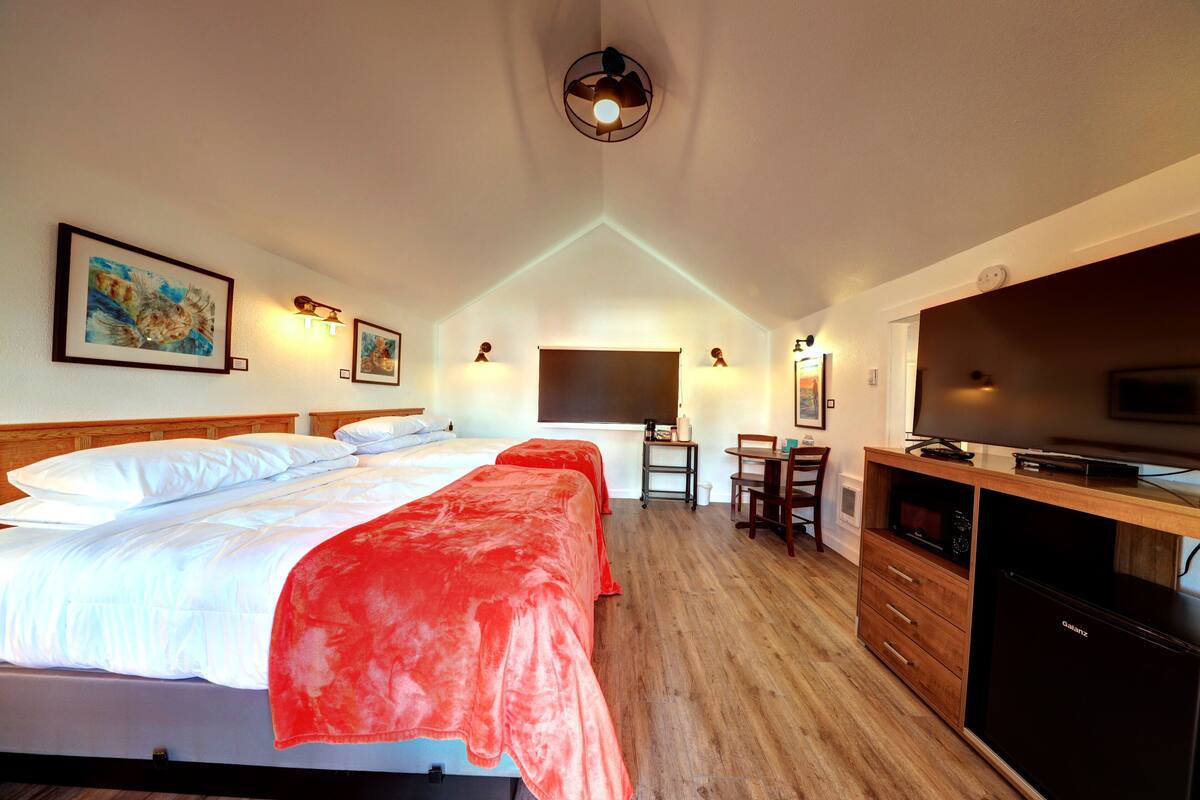 A hotel room with a bed, two bedside tables, a desk with a chair, a television, and a microwave.