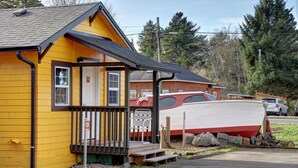 A yellow building with a porch, a white boat, and a red car parked nearby.