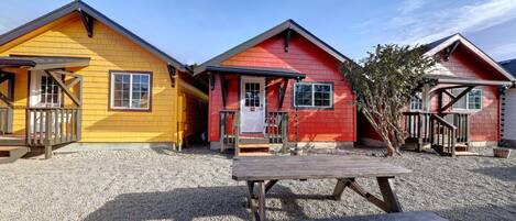 Three cabins with a gravel ground, a picnic table, and a wooden deck.