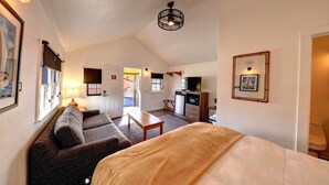 A compact room with a bed, a sofa, a small table, a kitchenette, and a door leading to another room.