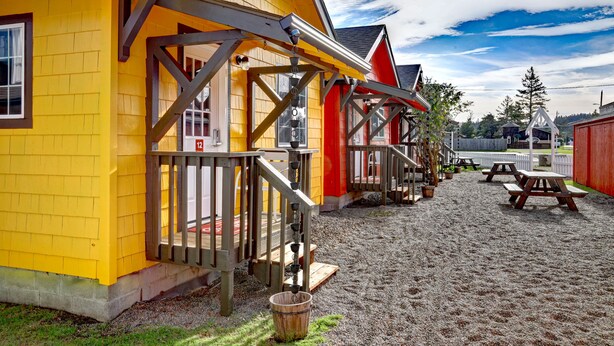 A yellow building with a wooden porch and picnic tables in a gravel area.