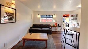 A living room with a sofa, a wooden coffee table, a small side table, and a bar area with stools.