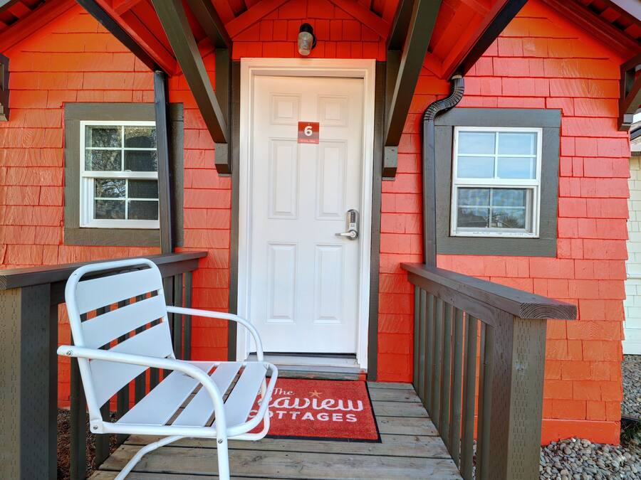 Um edifício vermelho com uma porta branca marcada com o número 6, uma cadeira branca e um tapete vermelho com o texto 'The Starview Cottages'.