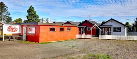 A row of small, single-story buildings with a gravel driveway and a white picket fence.