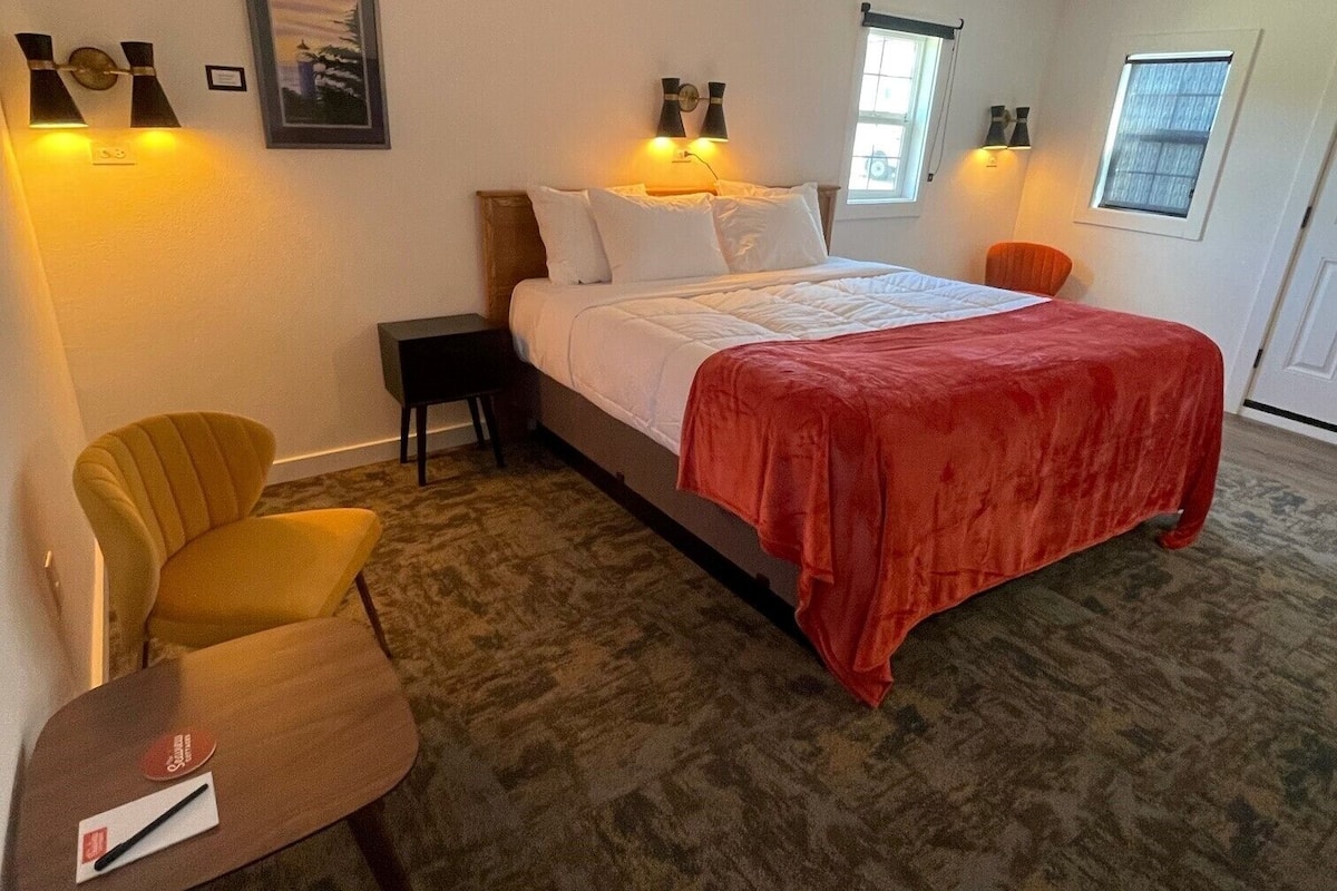 A hotel room with a bed, two chairs, a small table, and a window.