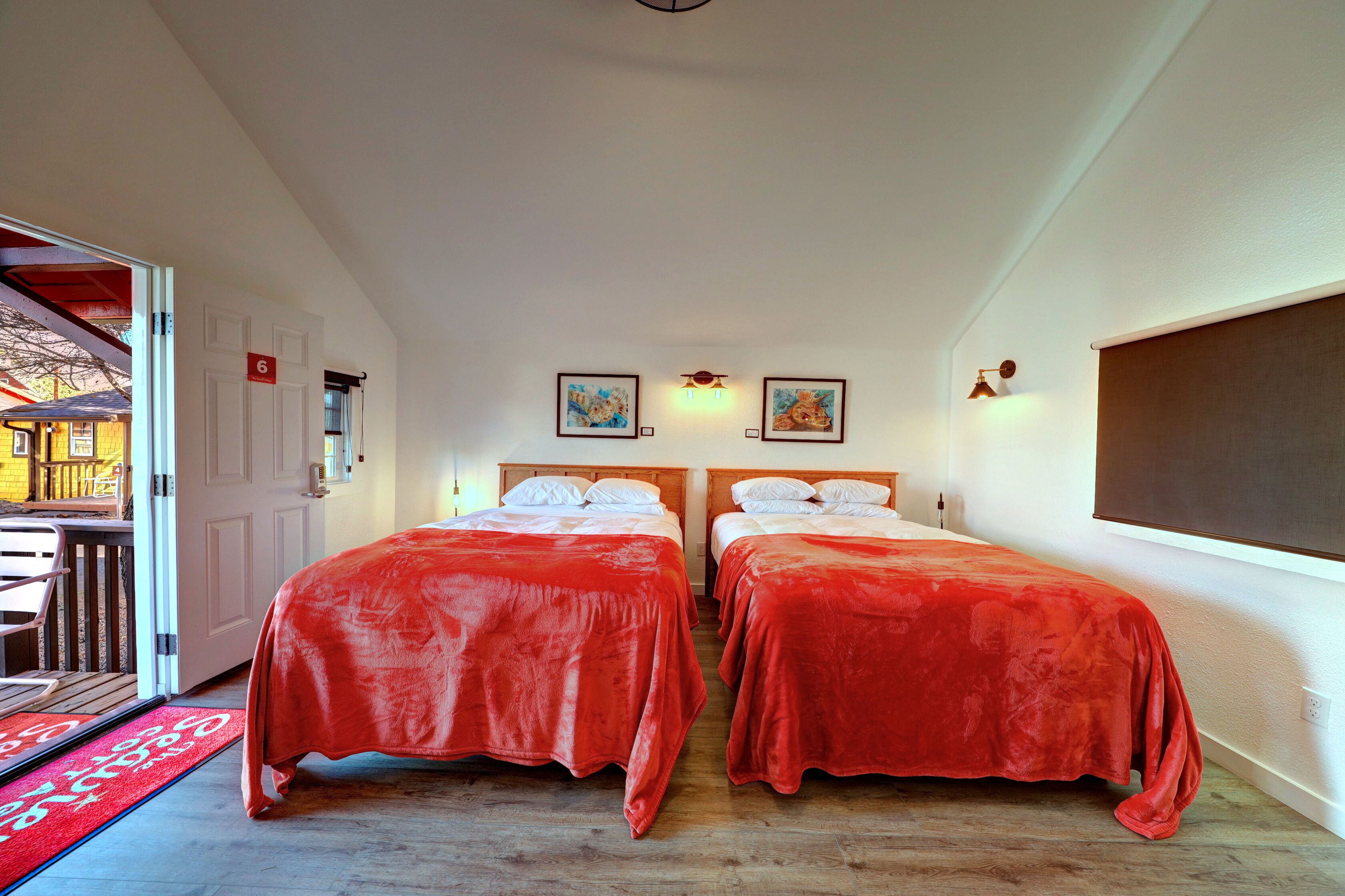 Una habitación de hotel con dos camas, suelo de madera, alfombra roja y un balcón con vistas.