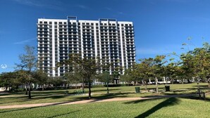 A high-rise building with a modern architectural design, surrounded by a well-maintained park with grass and trees. - Beautiful Condo at Downtown Doral! (Doral)