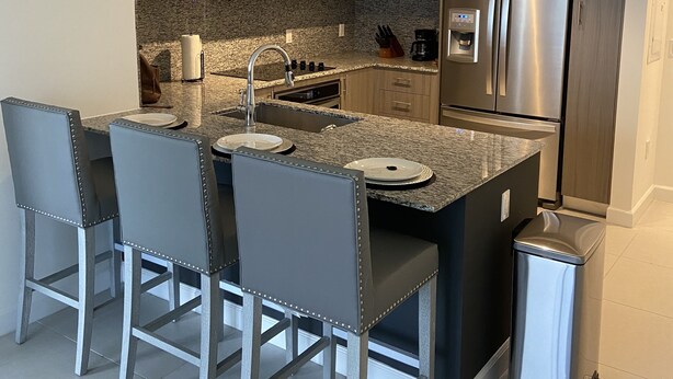A modern kitchen with a central island, stainless steel appliances, and bar stools. - Beautiful Condo at Downtown Doral! (Doral)