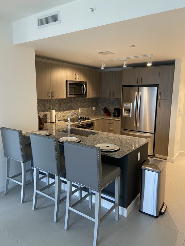 A modern kitchen with a central island, stainless steel appliances, and bar stools. - Beautiful Condo at Downtown Doral! (Doral)
