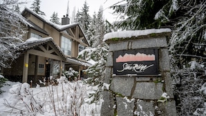 Ein Steinschild mit der Aufschrift 'Stowe Ridge', umgeben von schneebedeckten Bäumen und einer Lodge mit schrägem Dach.