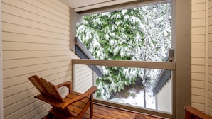 Ein Holzstuhl steht in einer Ecke des Raumes, dessen Wände mit weißen Profilbrettern verkleidet sind und ein großes Fenster auf eine verschneite Landschaft blickt.