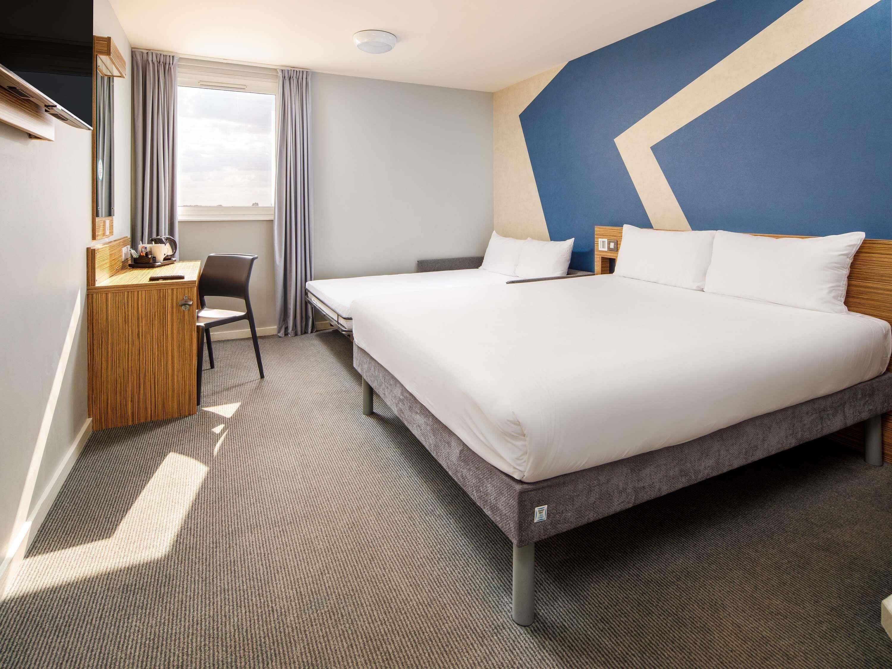 Une chambre d’hôtel avec un lit, un bureau, une chaise et une vue sur le ciel.