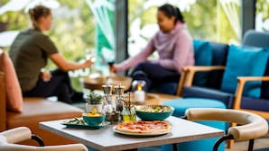 A dining area with a table set for two, a pizza, and a bowl of salad. - Ibis budget London Heathrow Central (Hounslow)