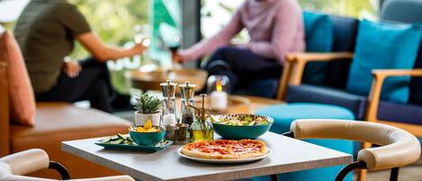 A dining area with a table set for two, a pizza, and a bowl of salad.