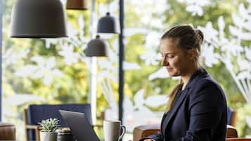 A person working on a laptop at a table with a coffee cup and a plant.