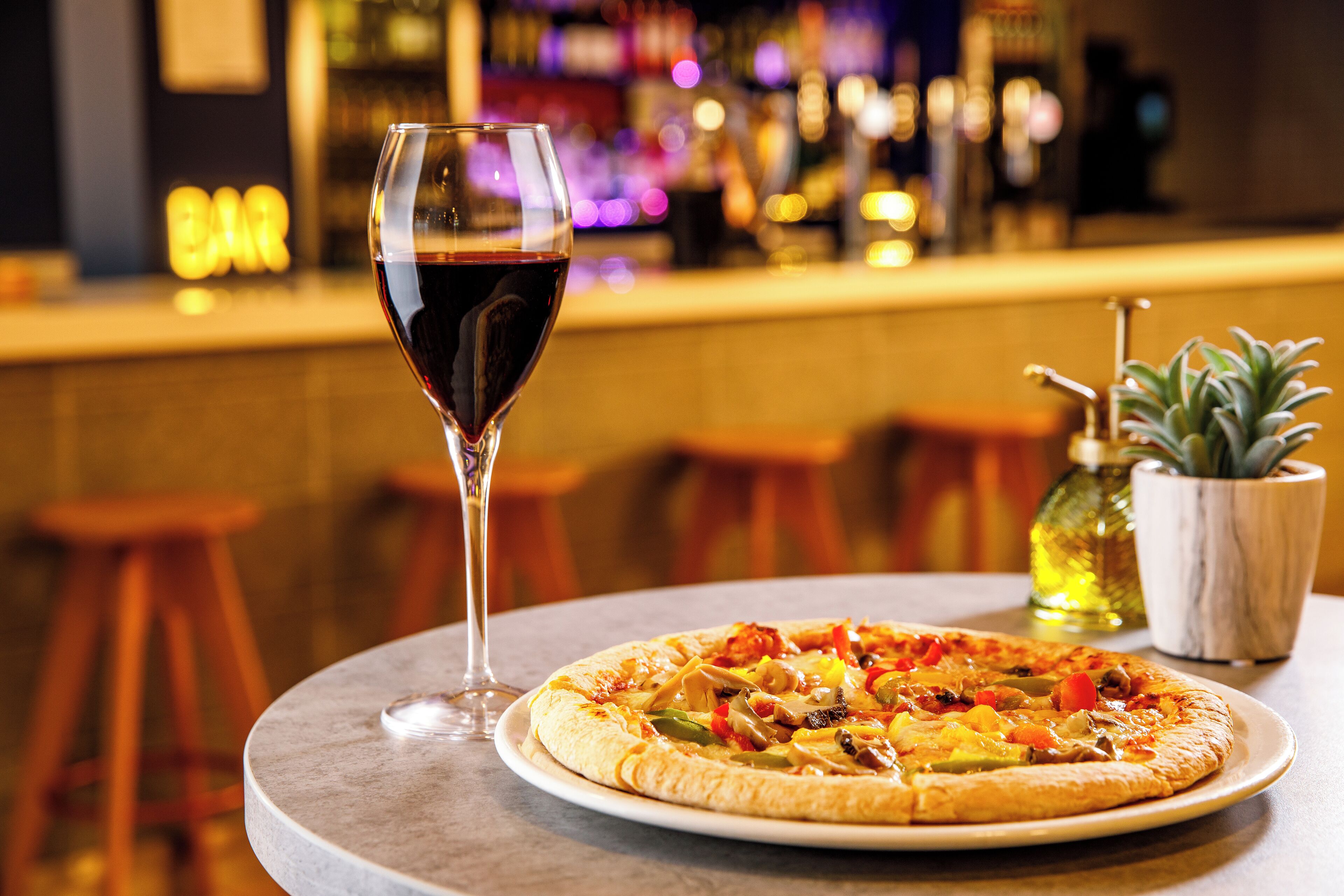 A pizza on a round table with a glass of red wine beside it.