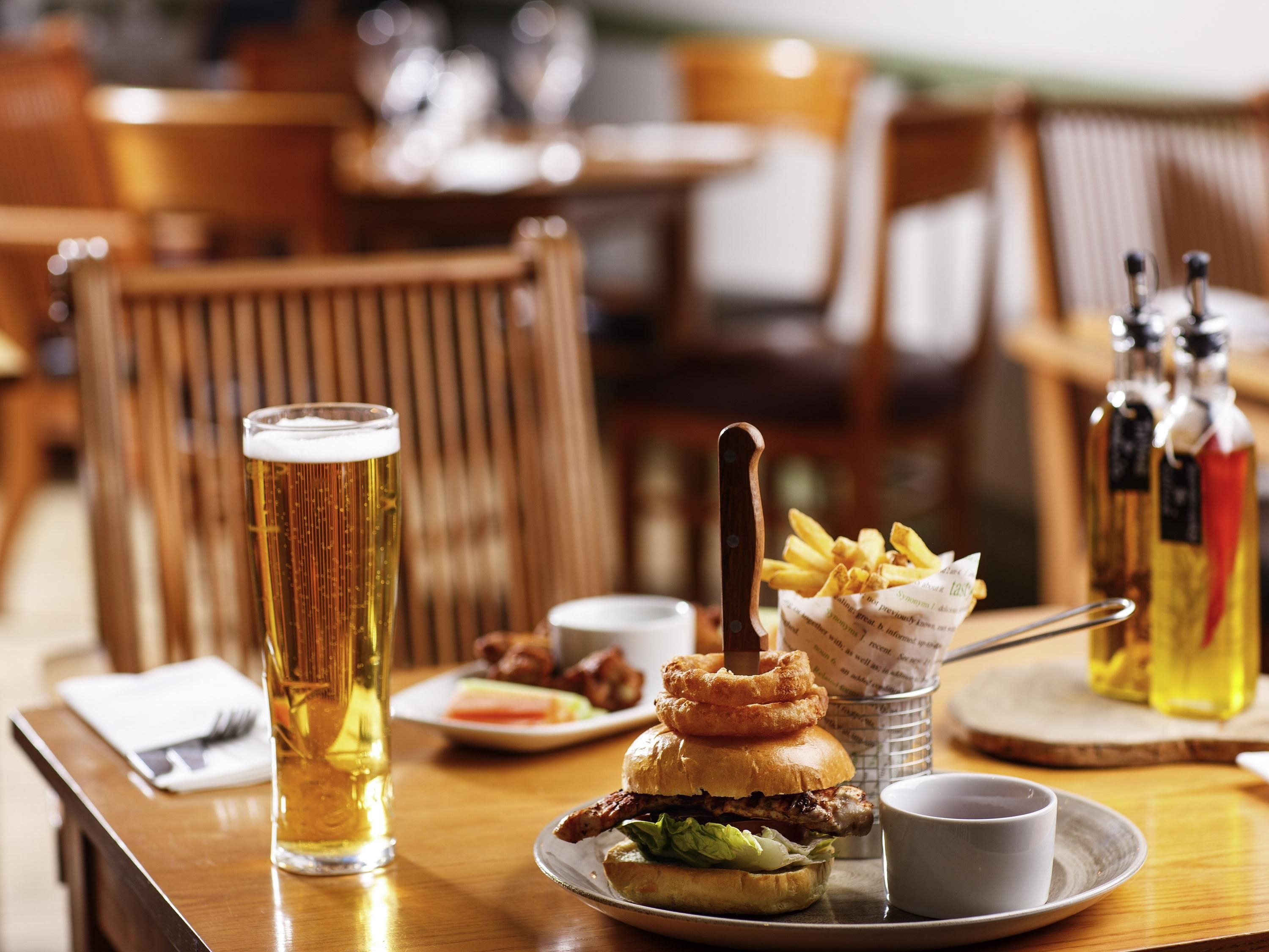 A dining table with a burger, fries, a glass of beer, and condiments.