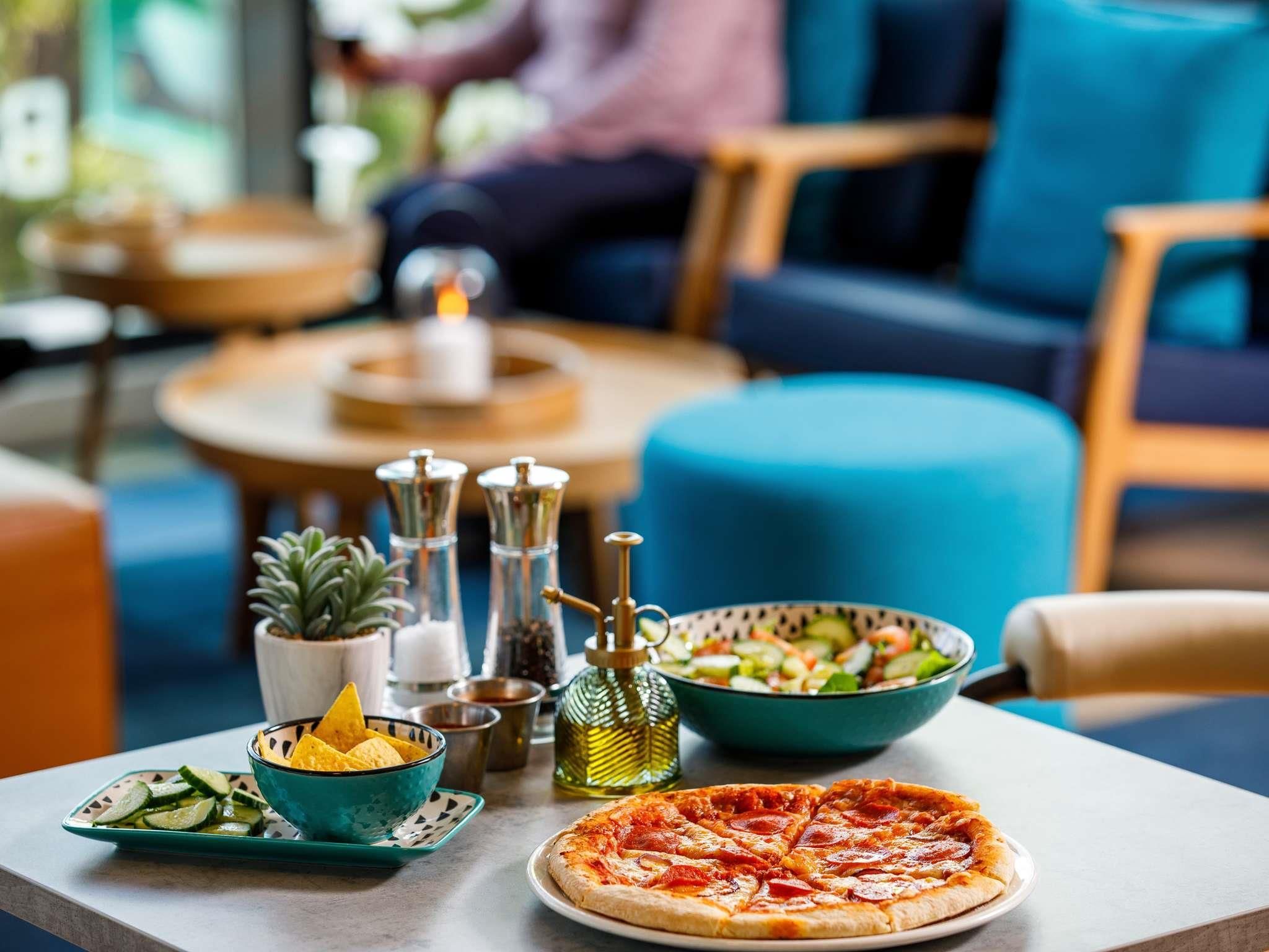 A dining table with a pizza, a bowl of salad, and condiments.