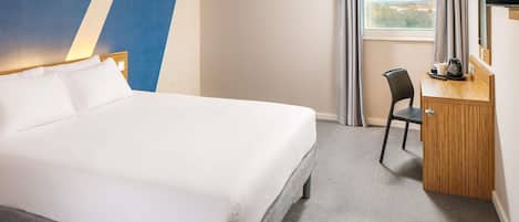 A hotel room with a bed, a desk, a chair, a TV, and a window with curtains.
